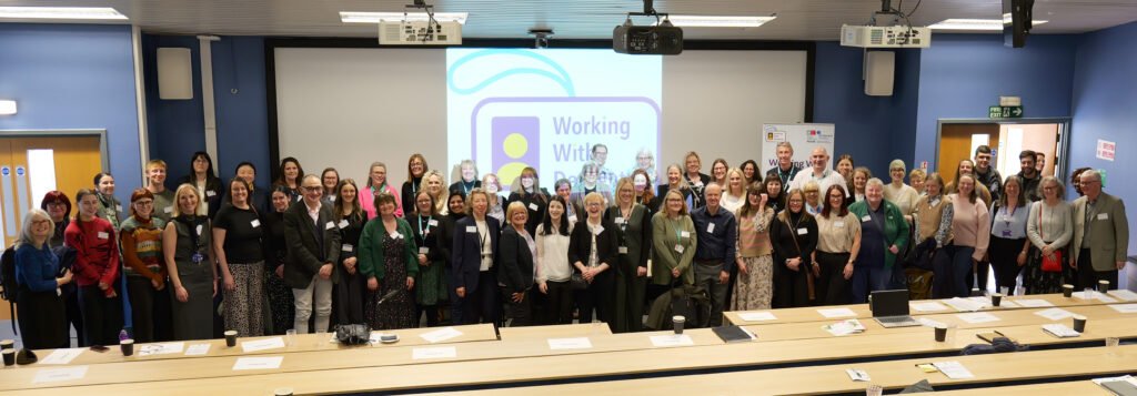 A photo of conference attendees and speakers across the front of the screen smiling at the camera.